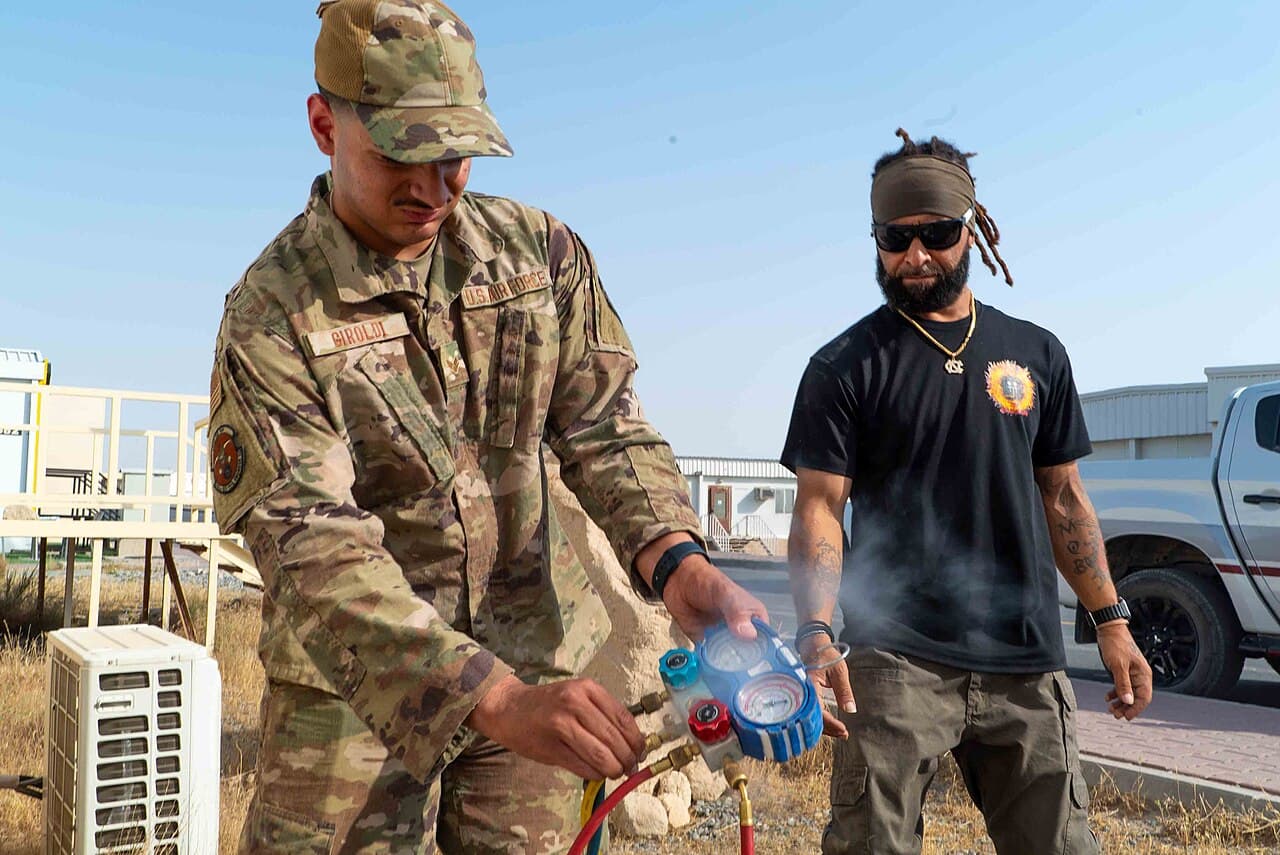 Two HVAC technicians reading a refrigerant manifold gauge set next to an outdoor air conditioning unit